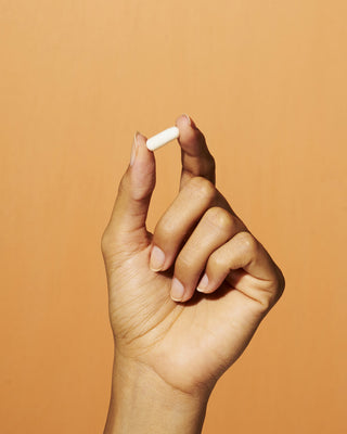 A hand holding a Tru Niagen supplement with an orange background.